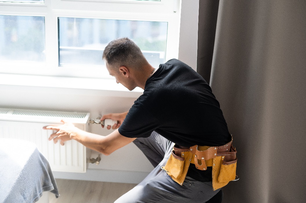 Ein junger Klempner überprüft einen Heizkörper während der Installation einer Heizungsanlage in einer Wohnung